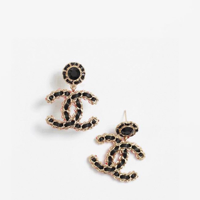 A pair of logo stud earrings in gold-tone metal with black enamel detailing and a central black stone, displayed on a clean white background.