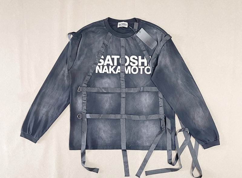 A dark gray long-sleeve shirt with a distressed, washed texture, featuring a white 'SATOSHI NAKAMOTO' graphic on the chest and multiple gray straps crossing the front. The shirt is laid flat on a light beige fabric background.