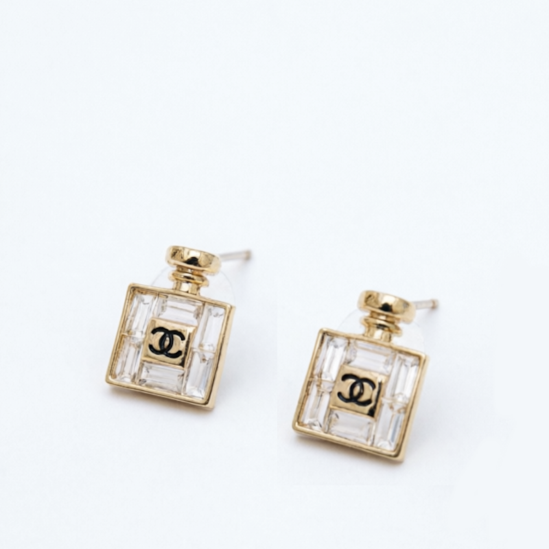 A pair of gold-toned stud earrings designed to look like a perfume bottle, featuring a clear faceted glass body with a black interlocking CC logo in the center.