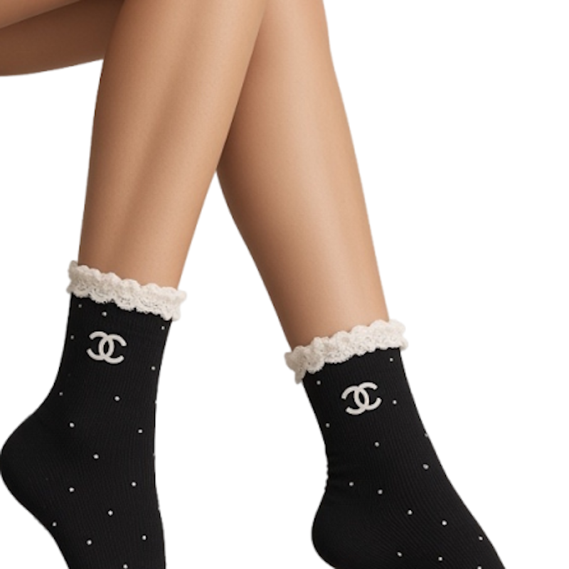 Black ankle socks with white polka dots, a white lace cuff, and a white embroidered C logo, shown on a model's legs against a white background.