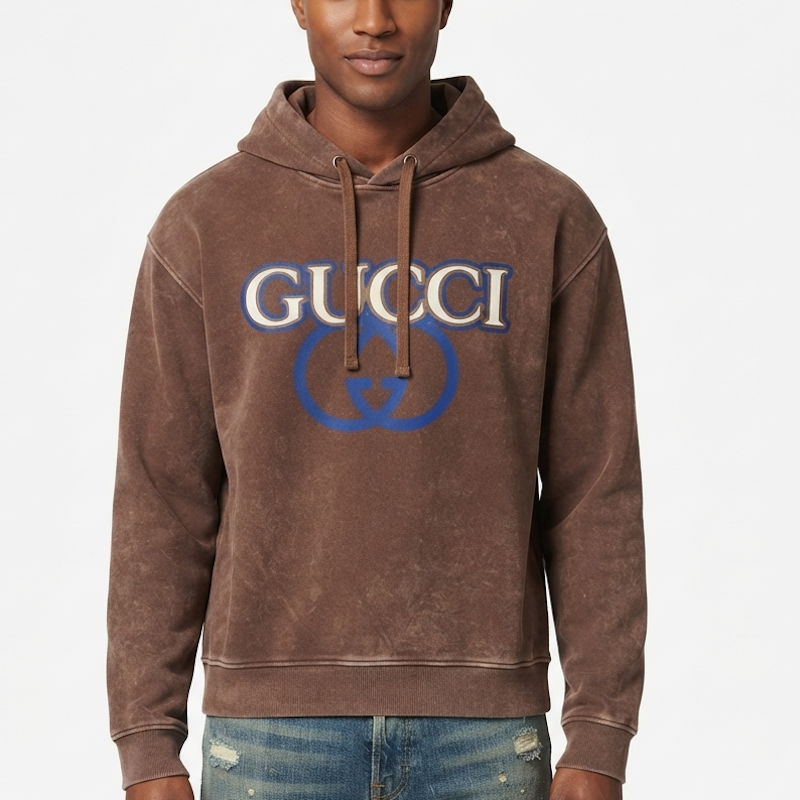 A man wearing a brown G hooded sweatshirt with a blue and white GG logo on the chest, paired with blue jeans, against a plain light gray background.