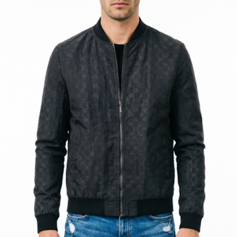 A man wearing a black bomber jacket with a subtle tonal monogram pattern, paired with blue jeans, shown against a plain white background.