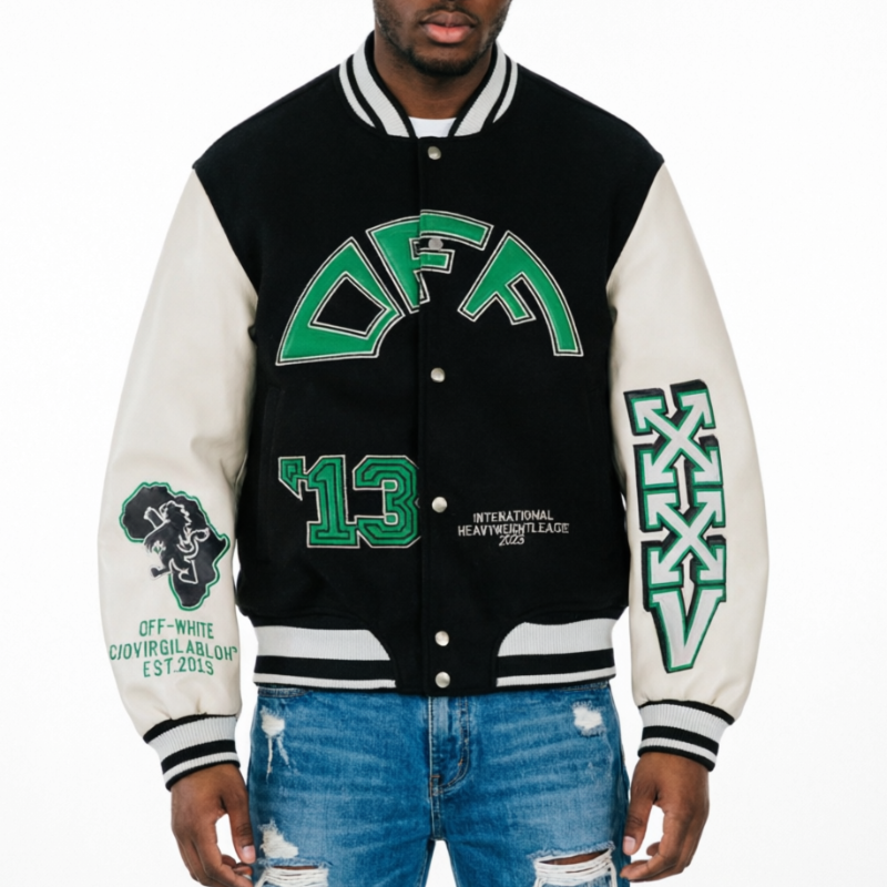 A man wearing a varsity-style jacket with a black body and off-white sleeves, featuring green collegiate lettering that reads 'DFA' and '13' on the front, plus additional green and black graphics on the sleeves, paired with distressed blue jeans against a plain white background.