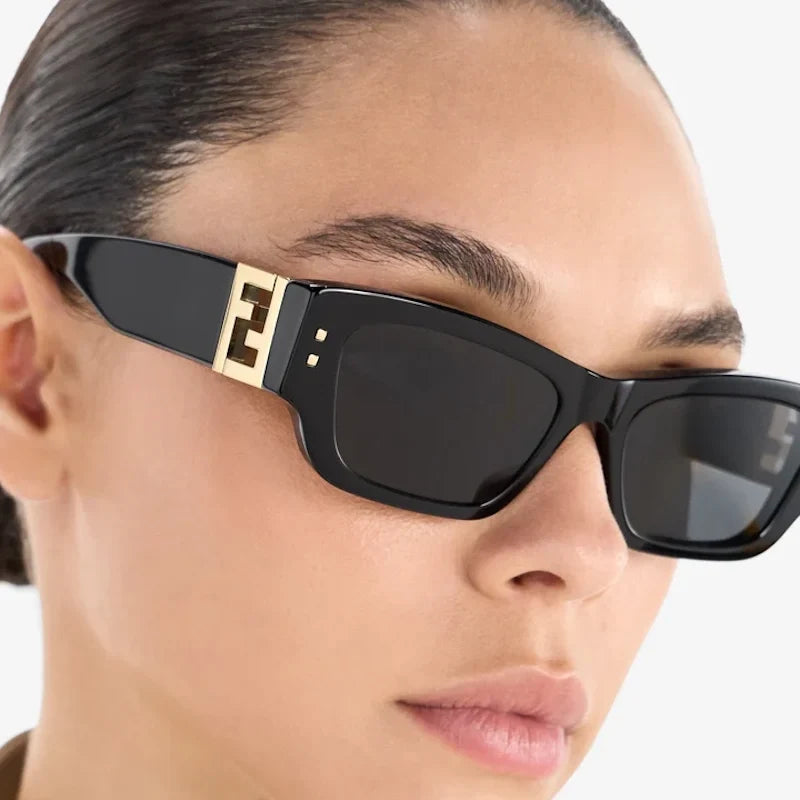 A close-up of a model wearing black cat-eye sunglasses with a gold double-F logo on the temple, indicating the brand Fendi.
