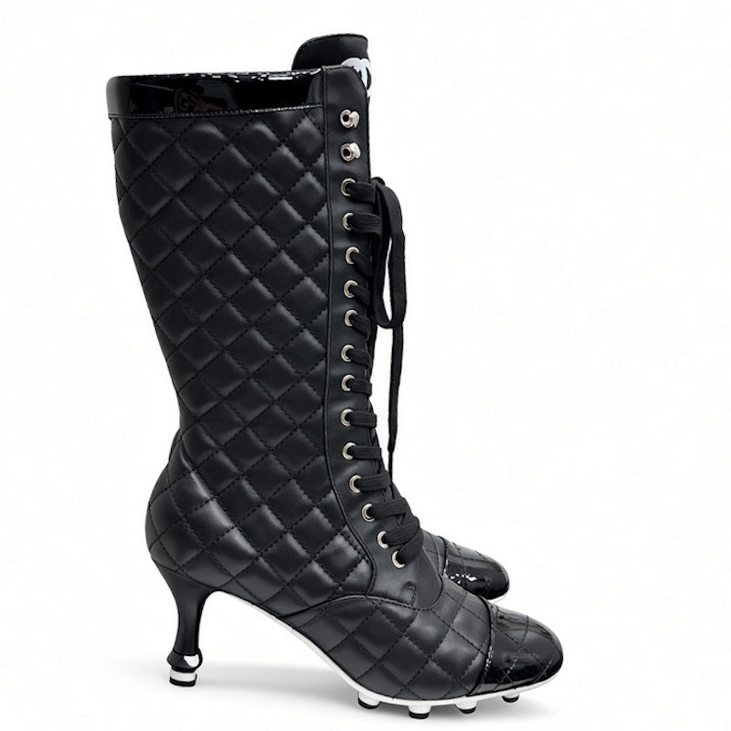 A black quilted knee-high boot with a pointed toe, kitten heel, and silver metal studs down the side, shown against a plain white background.