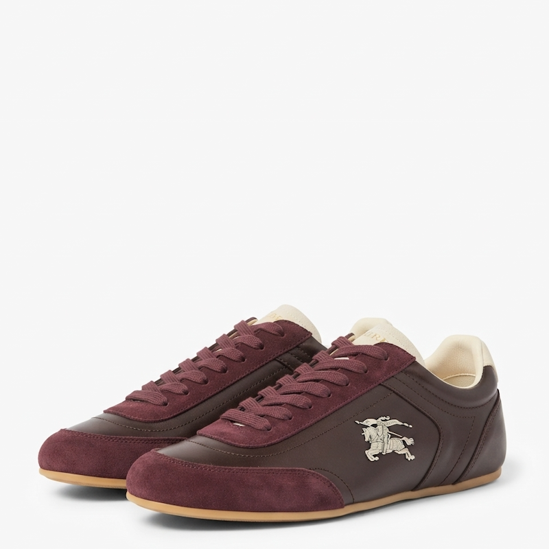 A pair of low-top sneakers in dark brown and burgundy suede, featuring a small silver knight emblem on the side, cream lining, and a tan outsole, shown against a light gray background.