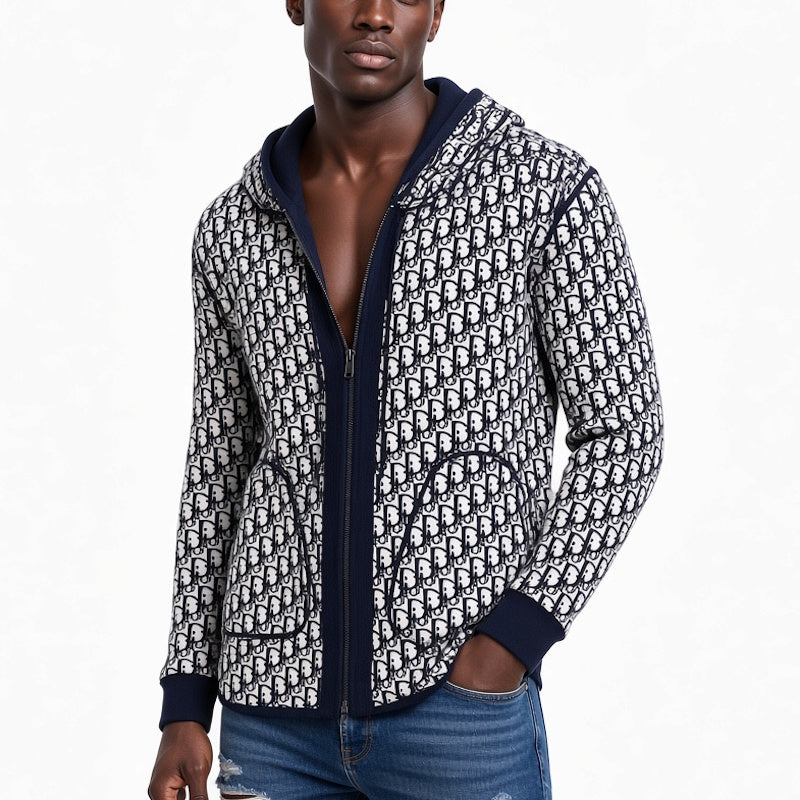 A man wearing a zip-up hoodie with a navy blue and white repeating monogram pattern, paired with blue jeans, against a plain white background.