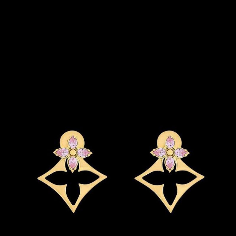 A pair of gold-tone earrings with a floral motif and pink gemstone accents, displayed on a solid black background.