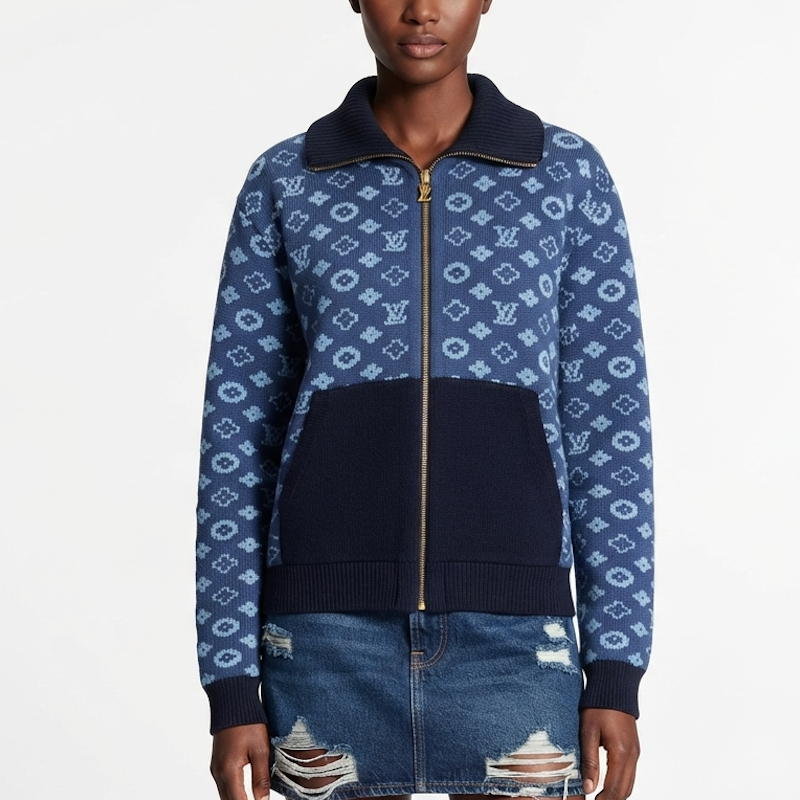 A model wearing a  zip-up jacket featuring a navy blue and light blue monogram pattern, a solid navy ribbed collar, and a solid navy front pocket, paired with a distressed denim skirt against a white studio background.