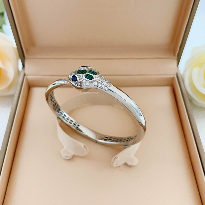 A silver snake ring with green and blue gemstone eyes and clear accent stones, displayed inside a beige jewelry box.