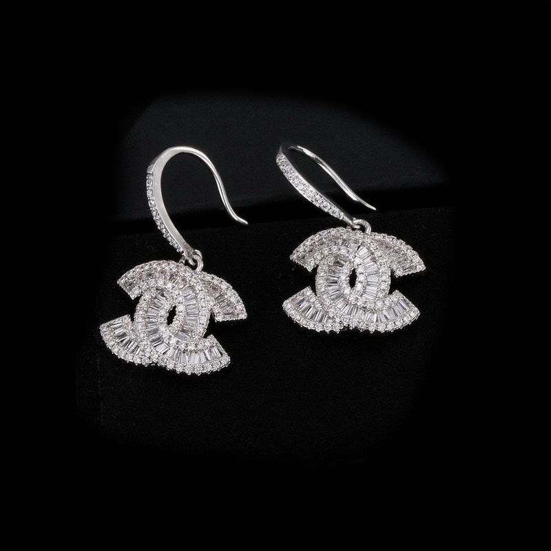 A pair of silver-toned drop earrings featuring a -style interlocking CC motif paved with clear stones, shown on a black background.
