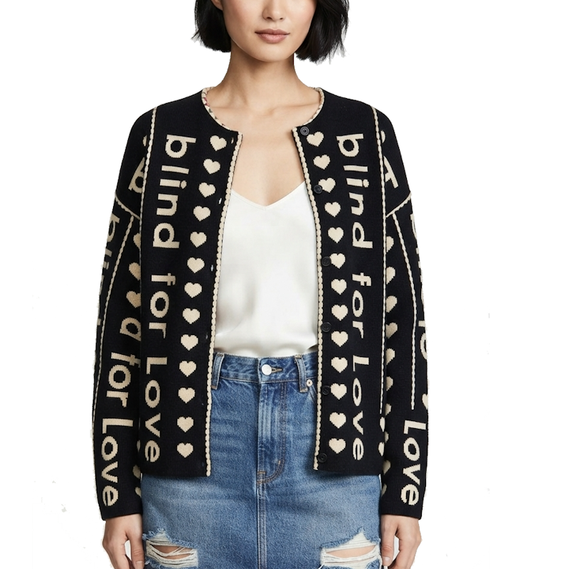 A woman wearing a black open-front cardigan with cream text reading 'blind for love' and cream hearts, styled over a white top and blue jeans against a plain white background.
