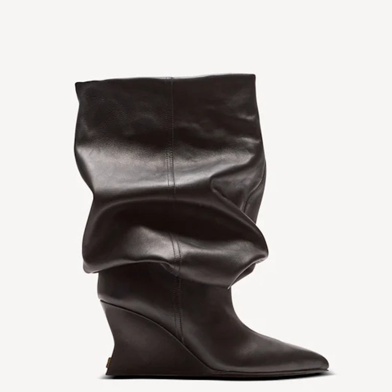 A single black leather mid-calf boot with a draped, slouchy silhouette, pointed toe, and wedge heel, shown against a plain light gray background.